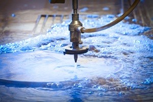 Waterjet cutting nozzle close-up from metalwork industry. CNC waterjet machine at work cutting a steel plate.